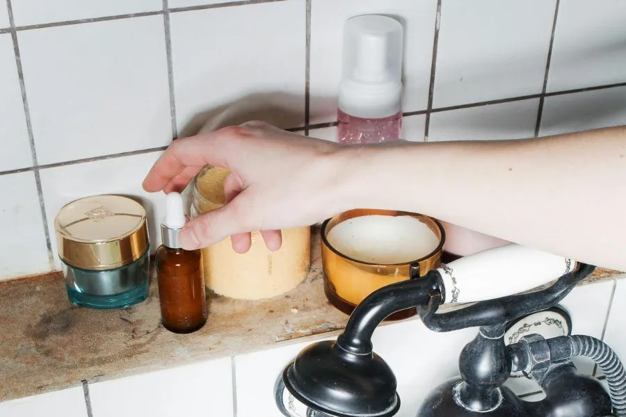 Hand reaching for cosmetics on a bathroom sink